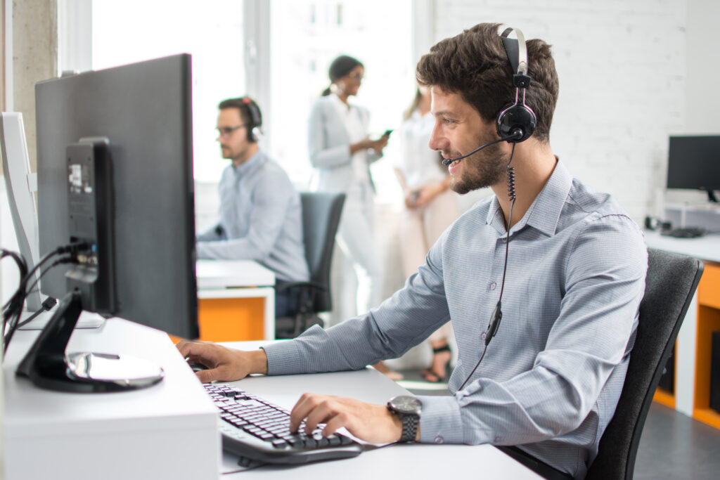 Smiling handsome customer support operator agent with hands-free device working in call center